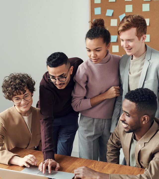 A diverse group of young professionals collaborating around a laptop in a modern office setting.